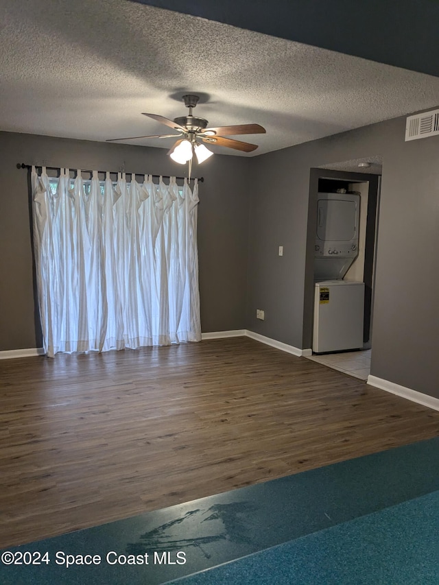 unfurnished room featuring hardwood / wood-style floors, ceiling fan, a textured ceiling, and stacked washer and clothes dryer