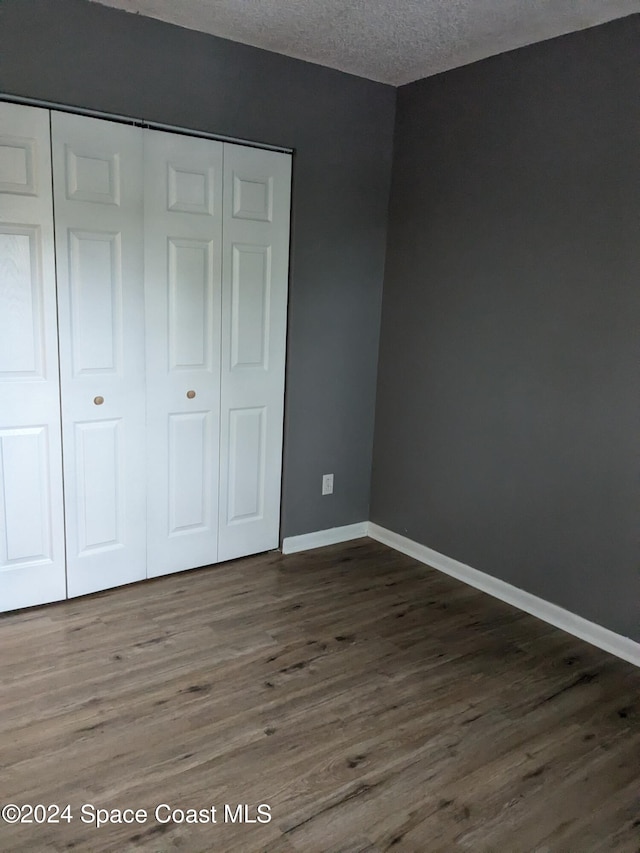 unfurnished bedroom featuring a textured ceiling, dark hardwood / wood-style flooring, and a closet