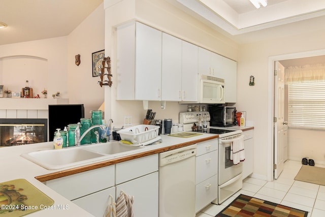 kitchen featuring white cabinetry, sink, white appliances, a tiled fireplace, and light tile patterned floors