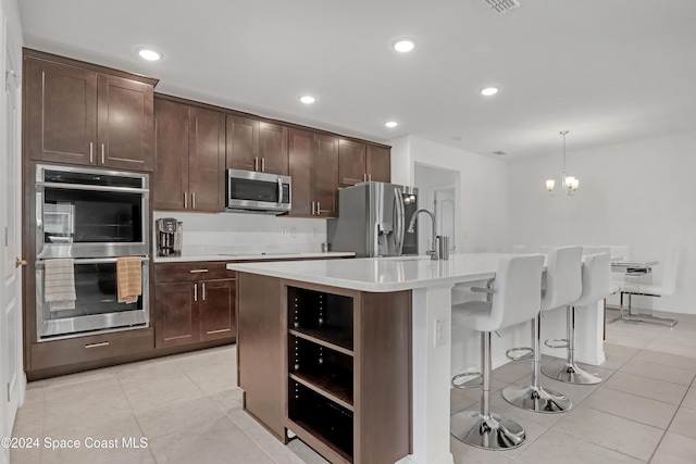 kitchen with pendant lighting, an island with sink, dark brown cabinetry, stainless steel appliances, and an inviting chandelier