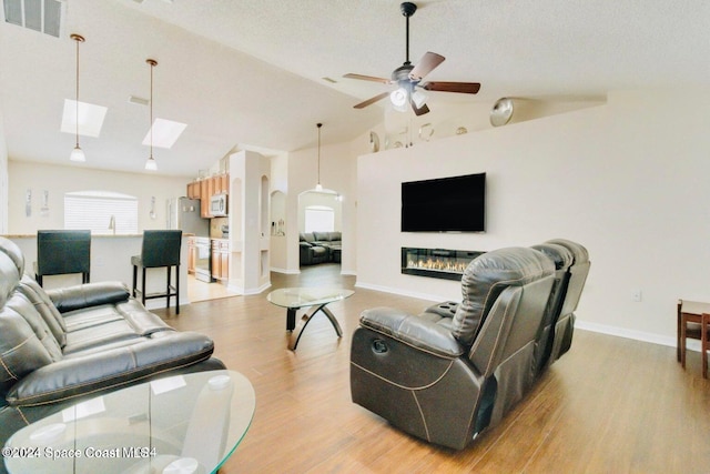 living room with ceiling fan, a textured ceiling, lofted ceiling, and light wood-type flooring