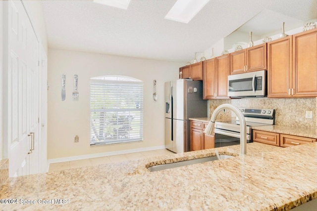 kitchen featuring light tile patterned floors, appliances with stainless steel finishes, tasteful backsplash, vaulted ceiling with skylight, and sink