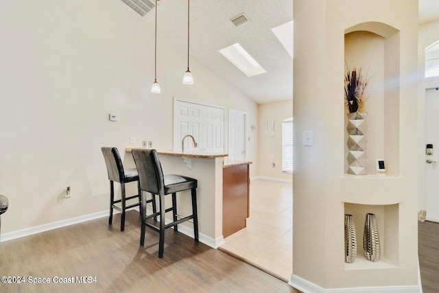 kitchen featuring kitchen peninsula, a kitchen breakfast bar, pendant lighting, light stone counters, and sink