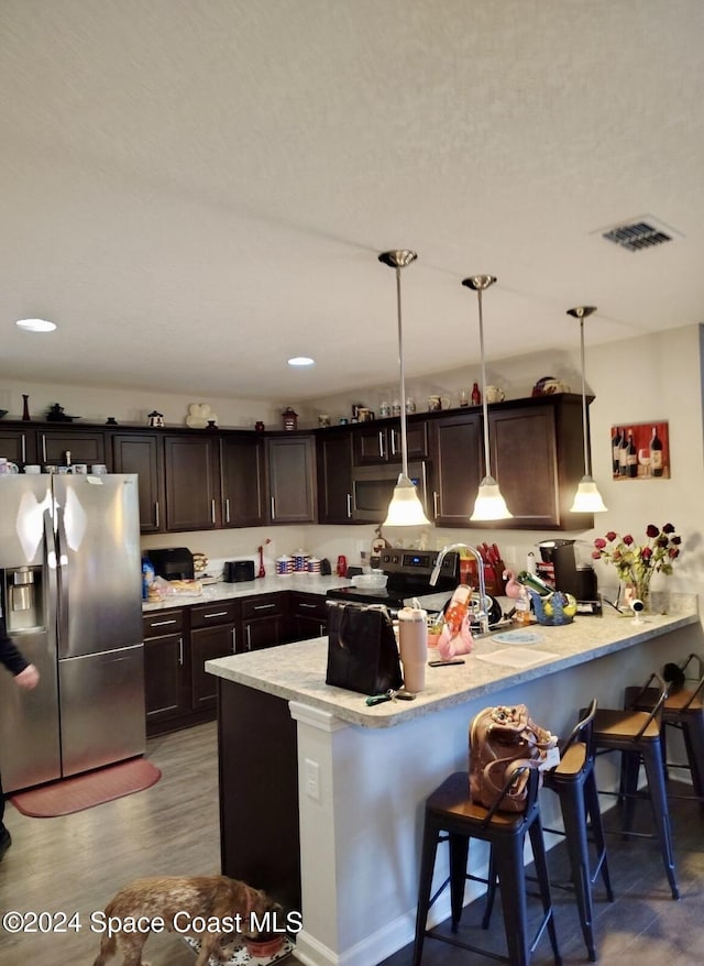 kitchen featuring kitchen peninsula, a breakfast bar, stainless steel appliances, hardwood / wood-style floors, and hanging light fixtures