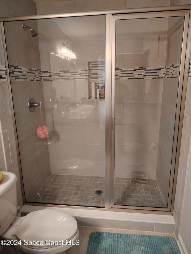 bathroom with tile patterned flooring, toilet, and a shower with shower door