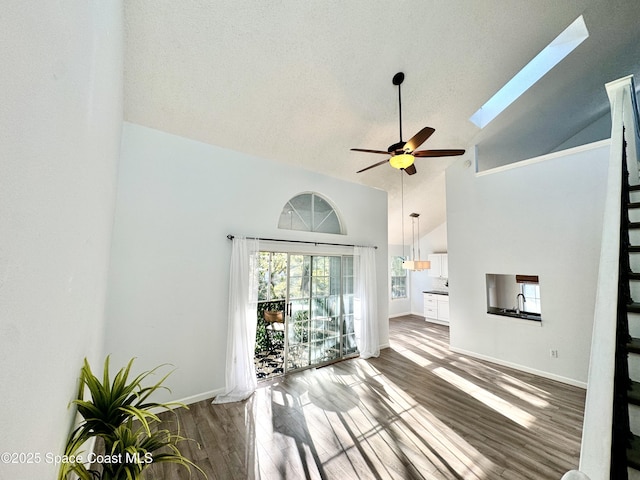 unfurnished living room with a skylight, a ceiling fan, wood finished floors, high vaulted ceiling, and baseboards