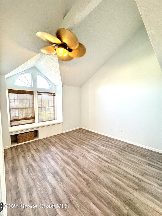 additional living space featuring a ceiling fan, vaulted ceiling, a textured ceiling, wood finished floors, and baseboards