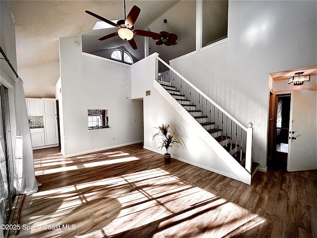 interior space with baseboards, ceiling fan, high vaulted ceiling, and wood finished floors