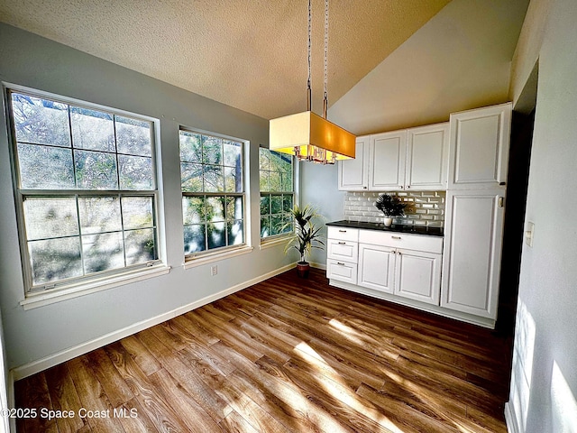 kitchen featuring dark countertops, lofted ceiling, hanging light fixtures, dark wood-type flooring, and white cabinetry