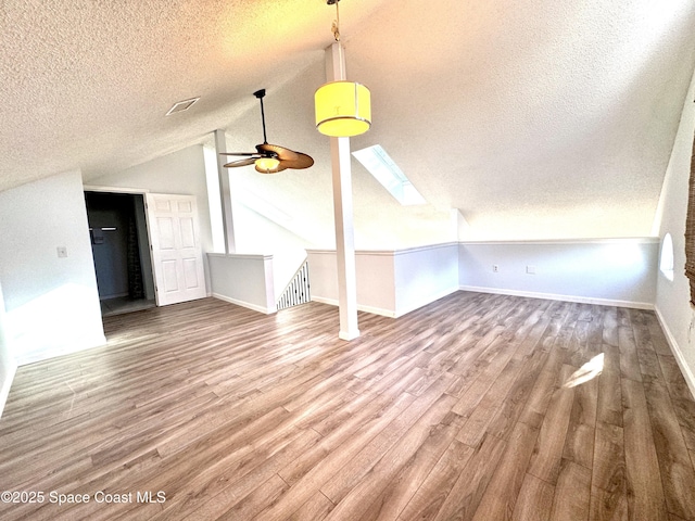 additional living space featuring a textured ceiling, wood finished floors, a ceiling fan, baseboards, and lofted ceiling with skylight