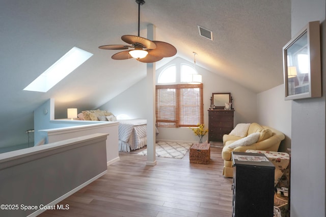 bedroom featuring visible vents, light wood-style floors, a textured ceiling, vaulted ceiling with skylight, and baseboards