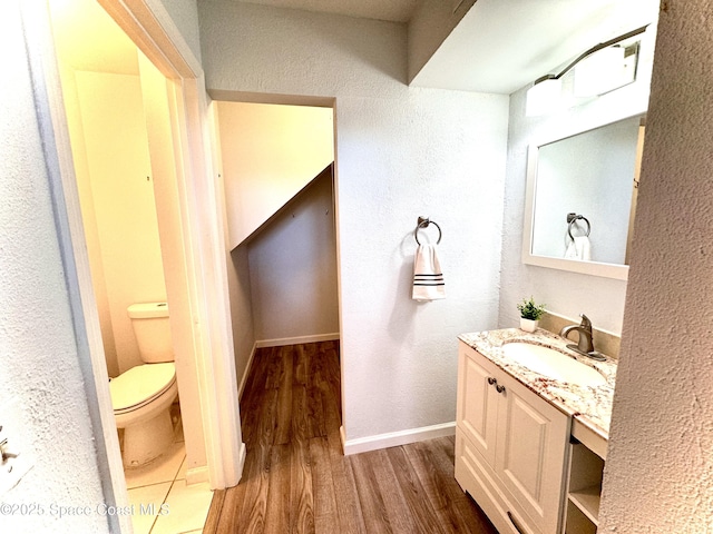 bathroom with baseboards, a textured wall, toilet, wood finished floors, and vanity