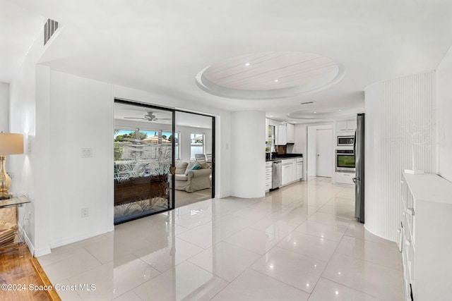 corridor featuring a tray ceiling, sink, and light tile patterned floors