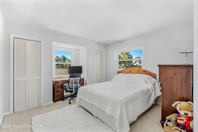 bedroom featuring light colored carpet, multiple windows, and multiple closets