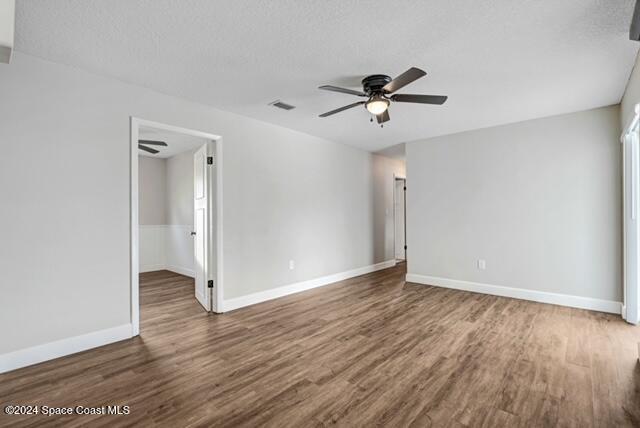 empty room with a textured ceiling, ceiling fan, and dark hardwood / wood-style floors