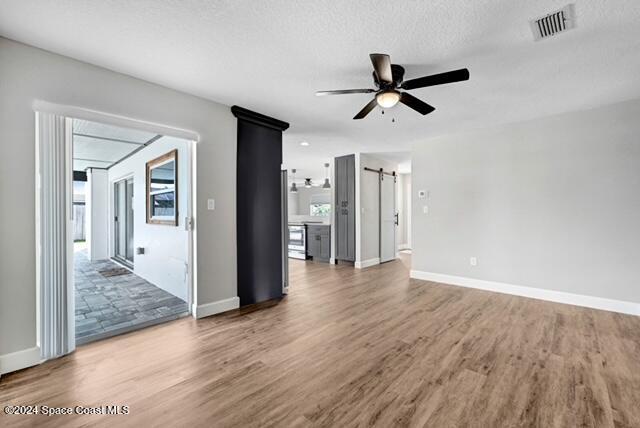 unfurnished living room featuring hardwood / wood-style floors, a barn door, a textured ceiling, and ceiling fan