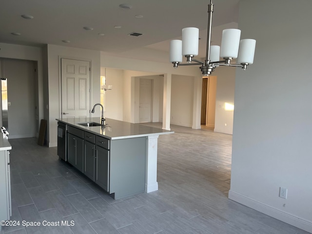 kitchen with dishwasher, sink, hardwood / wood-style flooring, an island with sink, and a notable chandelier