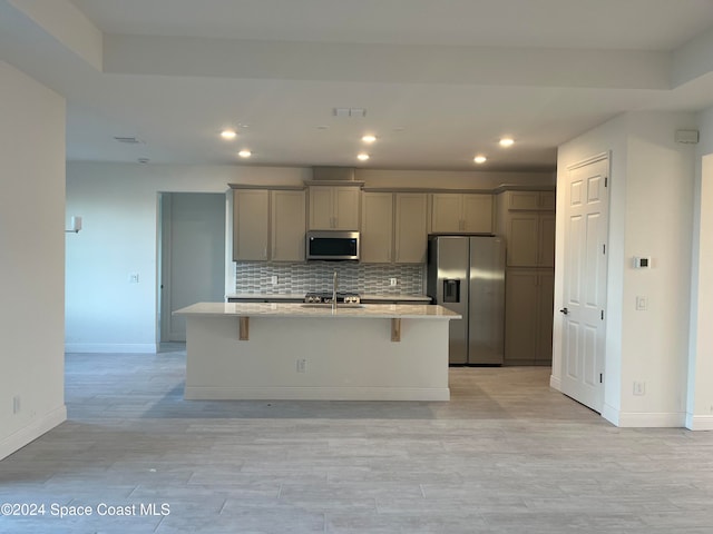 kitchen featuring a center island with sink, gray cabinets, stainless steel appliances, and tasteful backsplash