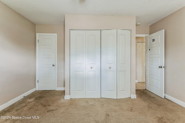 unfurnished bedroom featuring light carpet, a textured ceiling, and a closet