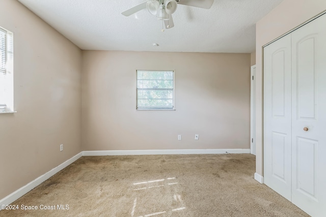 unfurnished bedroom with a textured ceiling, ceiling fan, light carpet, and a closet