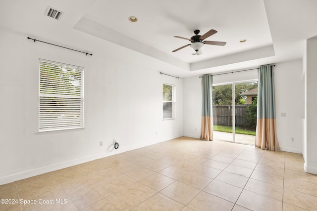 spare room with ceiling fan, a raised ceiling, light tile patterned floors, and a wealth of natural light