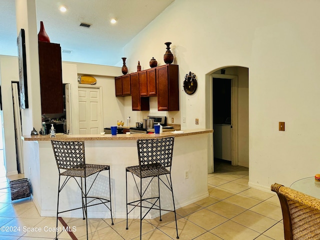 kitchen featuring kitchen peninsula, light tile patterned floors, high vaulted ceiling, and a breakfast bar area