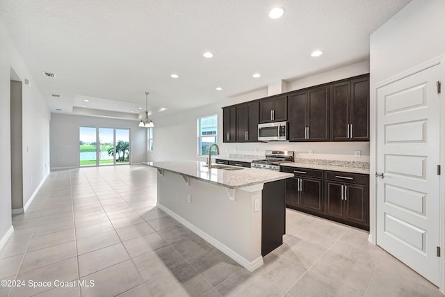 kitchen with appliances with stainless steel finishes, light stone counters, sink, a center island with sink, and a breakfast bar area