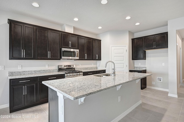 kitchen with a center island with sink, sink, light stone countertops, appliances with stainless steel finishes, and light tile patterned flooring