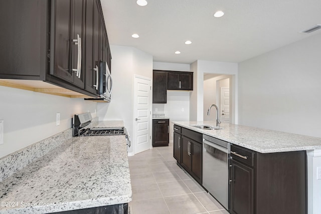 kitchen featuring sink, light stone countertops, light tile patterned floors, appliances with stainless steel finishes, and an island with sink