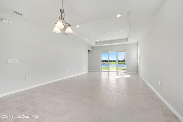 tiled spare room featuring a tray ceiling and a chandelier