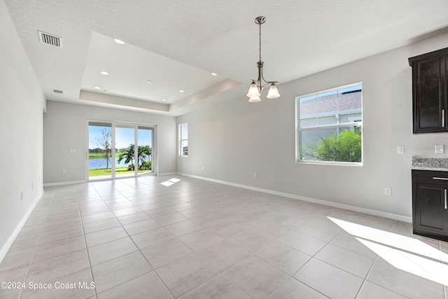 unfurnished living room featuring a chandelier, a water view, light tile patterned floors, and a tray ceiling