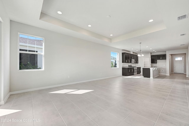 unfurnished living room with light tile patterned flooring, a wealth of natural light, and a tray ceiling