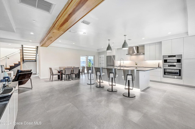 379 Hiawatha Way, Melbourne Beach, FL 32951 - kitchen with wall chimney range hood, modern cabinets, double oven, a kitchen bar, and white cabinetry