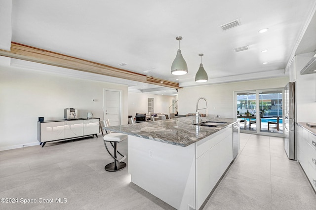 kitchen with pendant lighting, a kitchen island with sink, white cabinets, sink, and appliances with stainless steel finishes