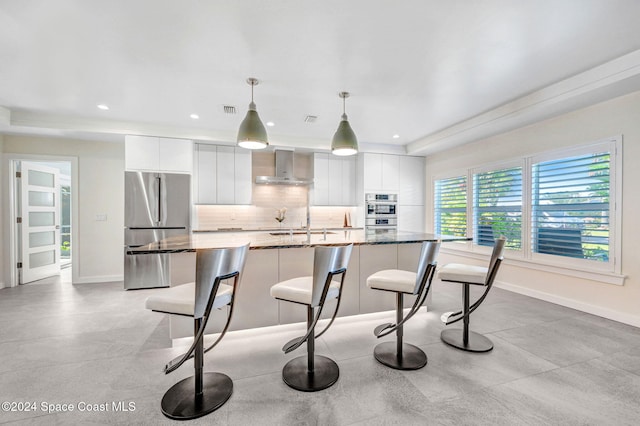 kitchen with white cabinets, wall chimney range hood, stainless steel appliances, and hanging light fixtures