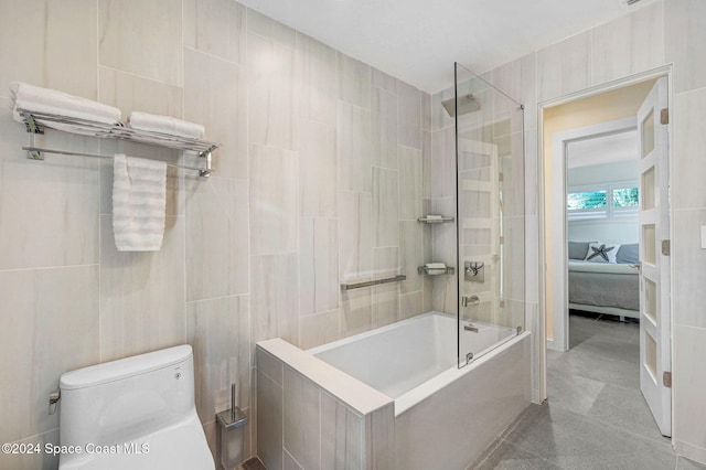 bathroom featuring tiled shower / bath, toilet, and tile walls