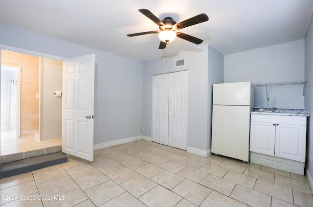 unfurnished bedroom with ceiling fan, sink, white fridge, a closet, and light tile patterned floors