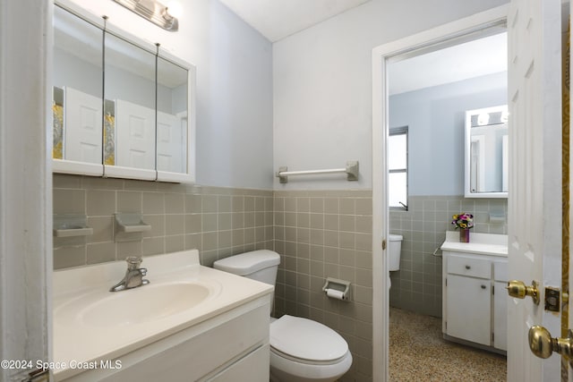 bathroom featuring vanity, toilet, and tile walls