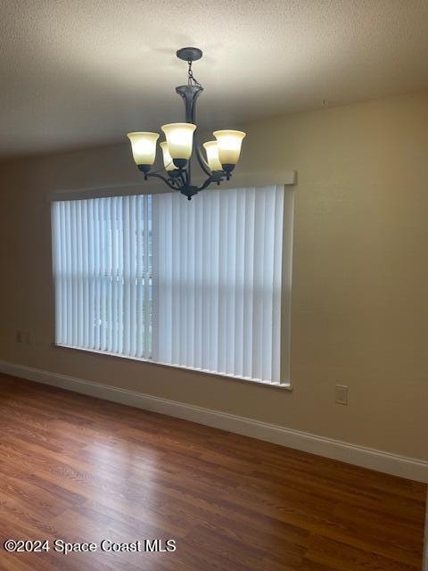 empty room featuring dark hardwood / wood-style flooring, a textured ceiling, and a notable chandelier