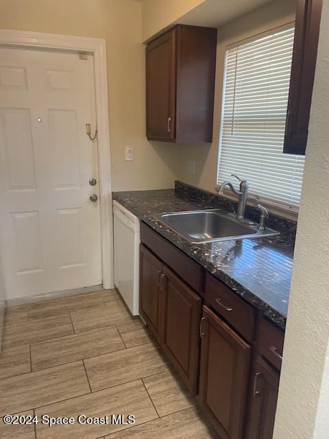 kitchen featuring dark stone countertops, sink, white dishwasher, and dark brown cabinets