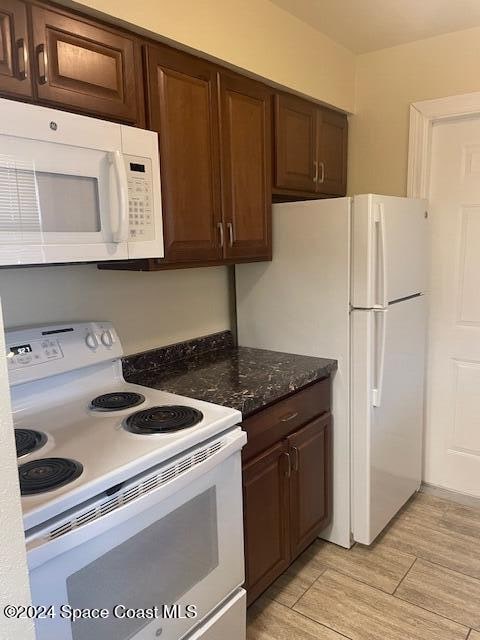 kitchen featuring dark brown cabinets, white appliances, and dark stone counters