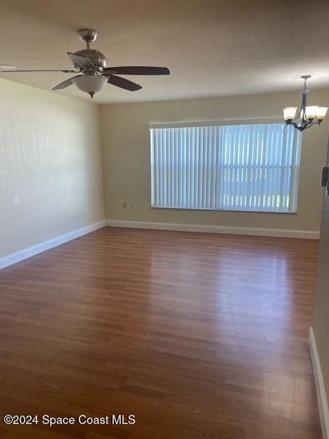 unfurnished room with dark hardwood / wood-style flooring, a healthy amount of sunlight, and ceiling fan with notable chandelier