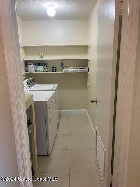 laundry area featuring separate washer and dryer, a textured ceiling, and light tile patterned floors