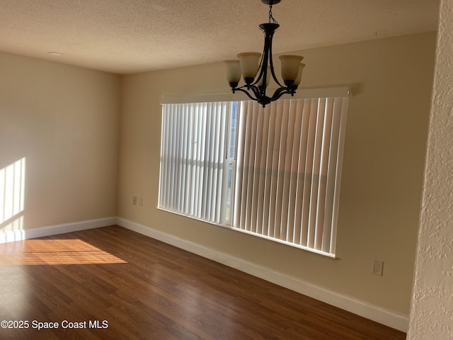 unfurnished room featuring dark hardwood / wood-style flooring, a textured ceiling, and a chandelier