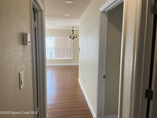 hallway featuring hardwood / wood-style flooring, a textured ceiling, and an inviting chandelier