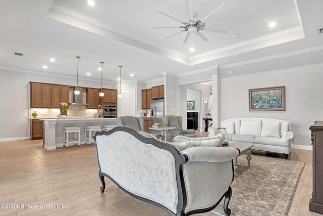 living room featuring a raised ceiling, ceiling fan, and light hardwood / wood-style floors