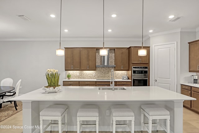 kitchen featuring double oven, a breakfast bar, decorative light fixtures, and wall chimney range hood