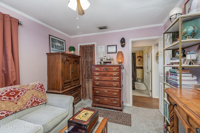 living area featuring ceiling fan, crown molding, light colored carpet, and a textured ceiling