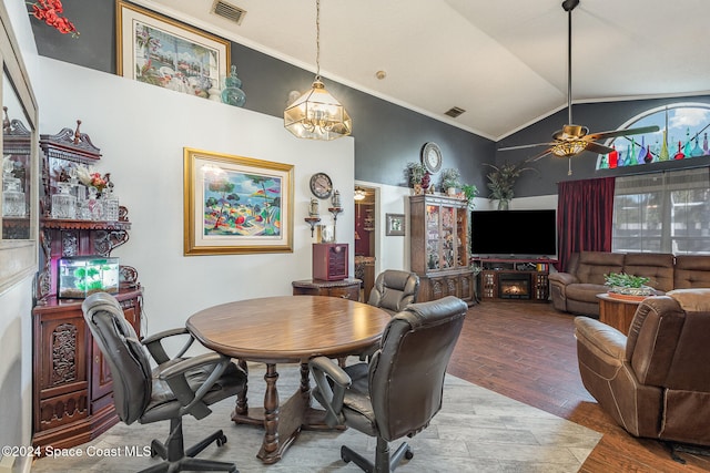 dining room with high vaulted ceiling, ceiling fan with notable chandelier, hardwood / wood-style flooring, ornamental molding, and a fireplace