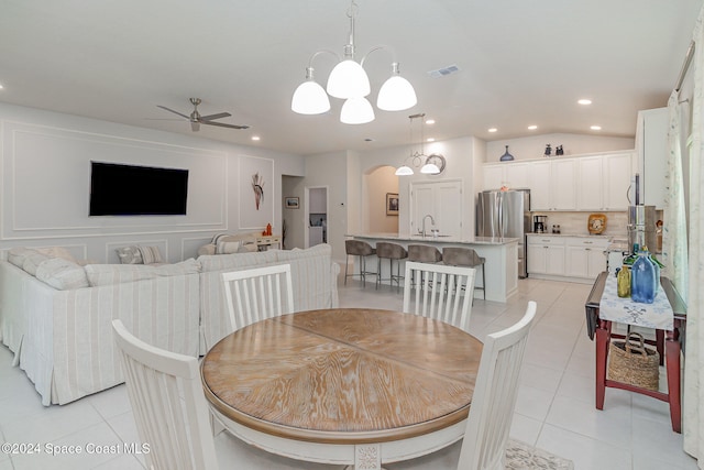 dining space with ceiling fan with notable chandelier, light tile patterned floors, sink, and vaulted ceiling